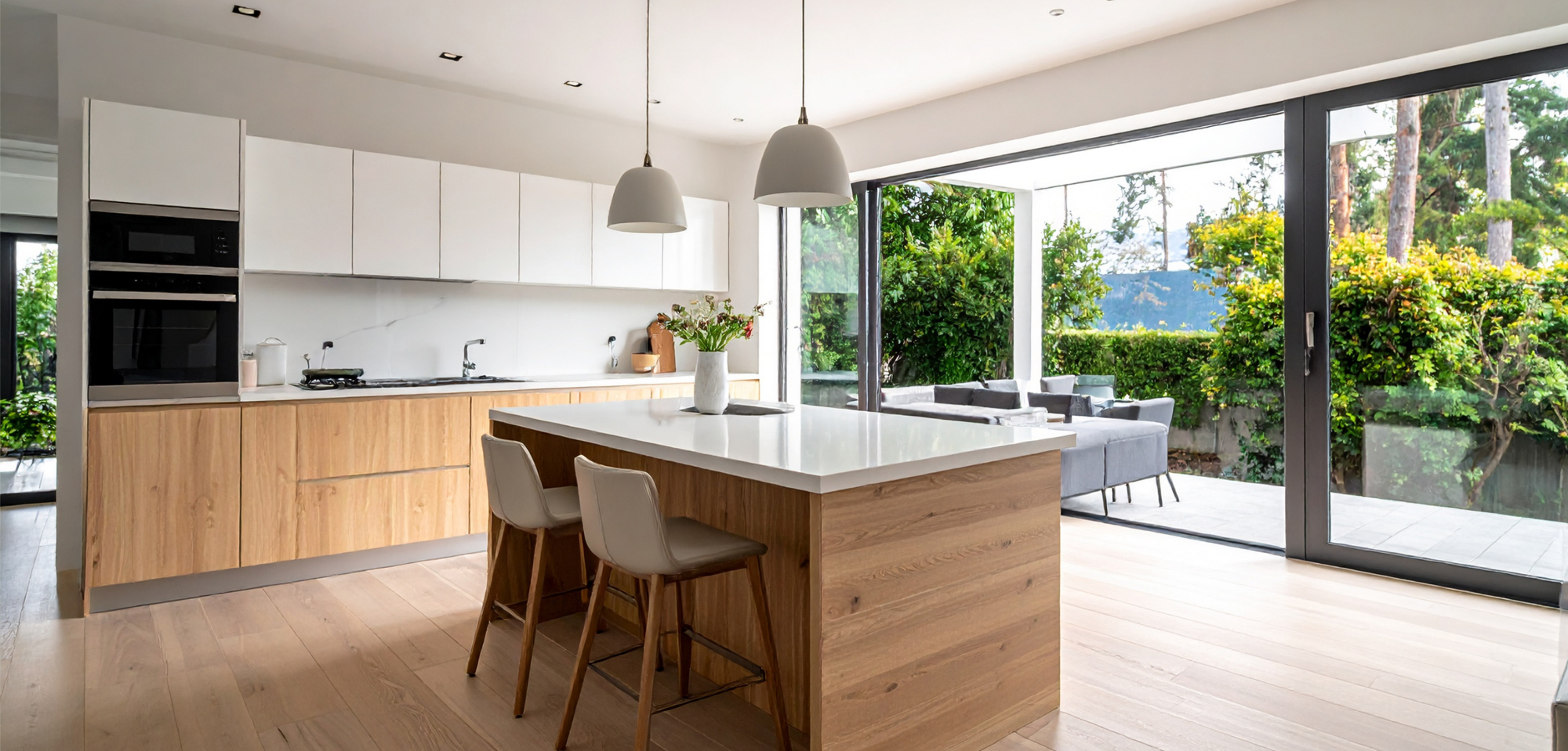 Bright residential kitchen featuring natural wood cabinets, white quartz countertops, and large sliding glass doors.